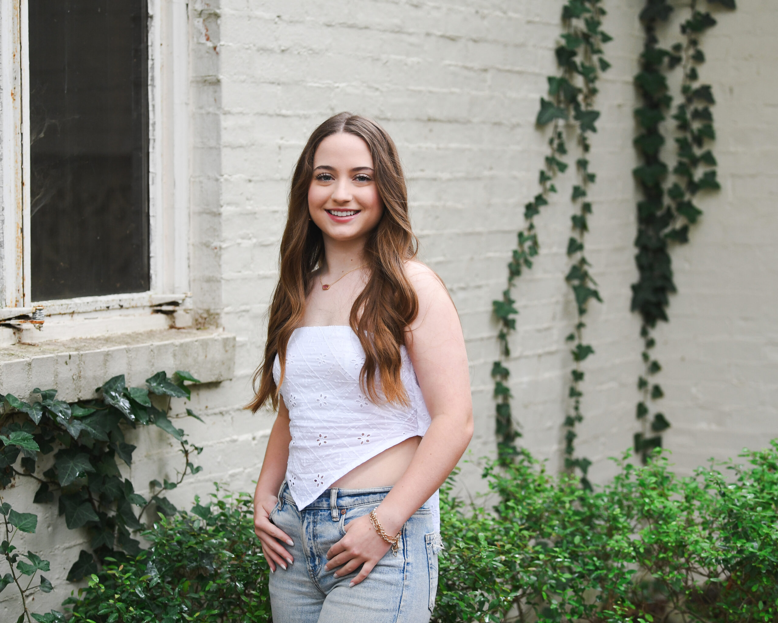 Senior photos near white bricks and green vines.